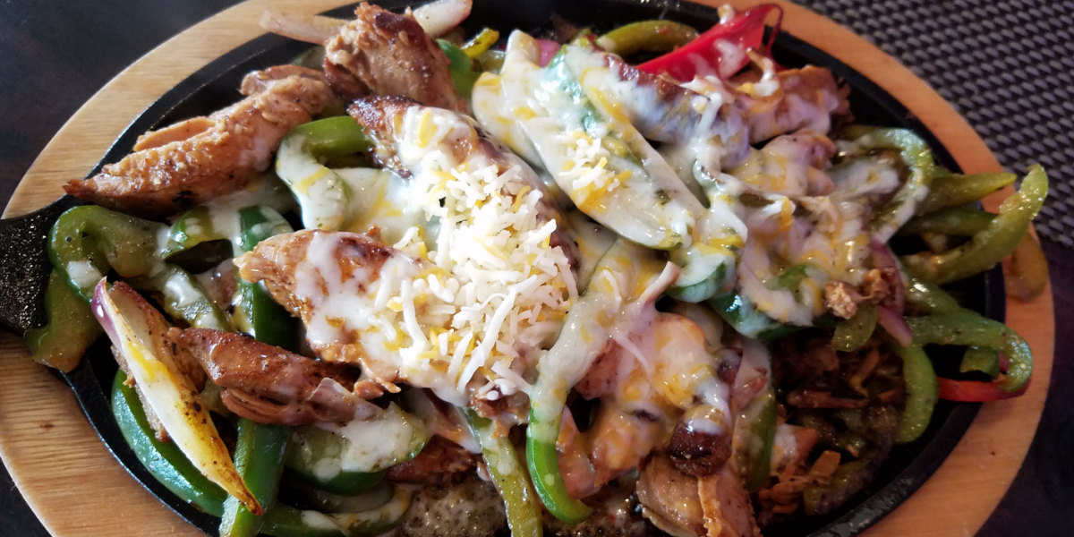 Bell Peppers, Unstuffed Recipe Photo. Meat and bell peppers covered in cheese. Background is black, with a circle of wood around outside of the plate.