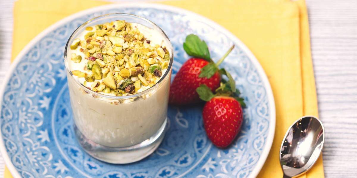 Berries and Pistachio Parfait Recipe Photo. Cup of yogurt is in a blue plate with some berries next to it; under the plate is a yellow napkin. Background is light grey.