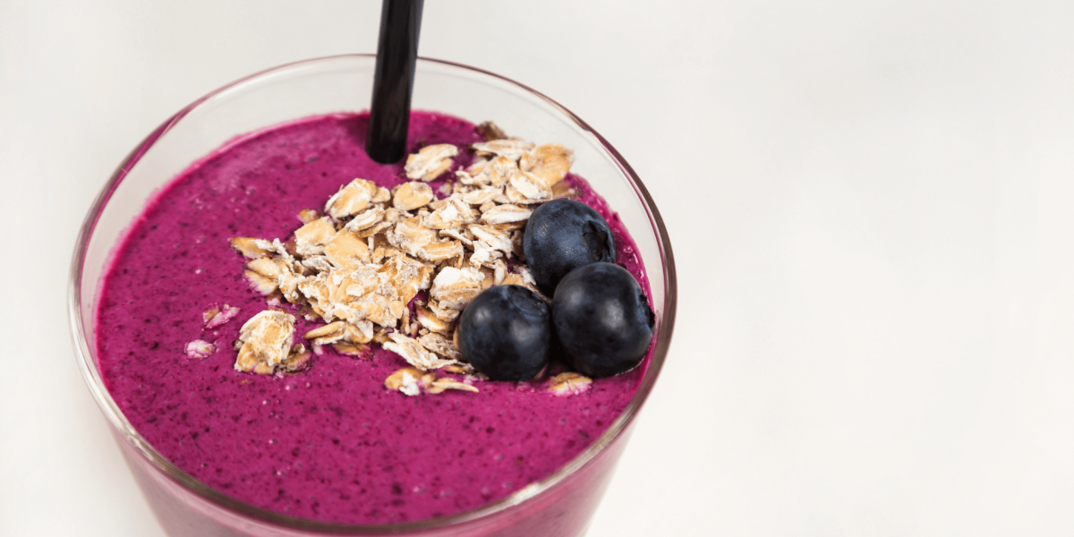 Smoothie with blueberries, oats, milk, hemp seeds, and banana. Against a white background.