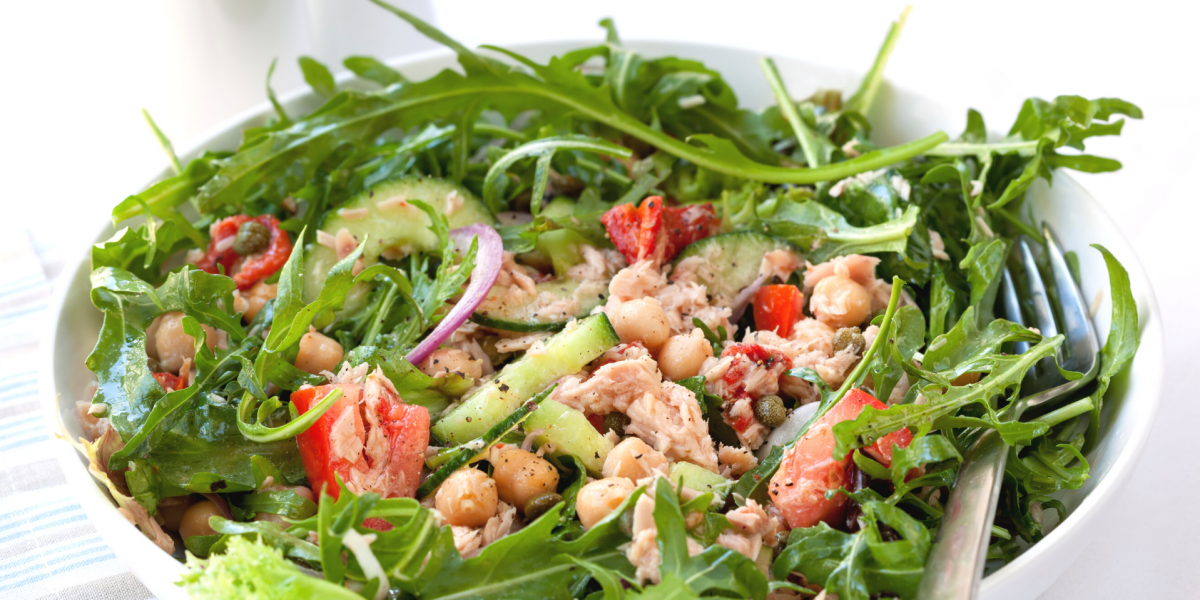 Chickpea Tuna Salad in a white bowl, against a white background. Salad also contains greens, tomatoes and other vegetables.