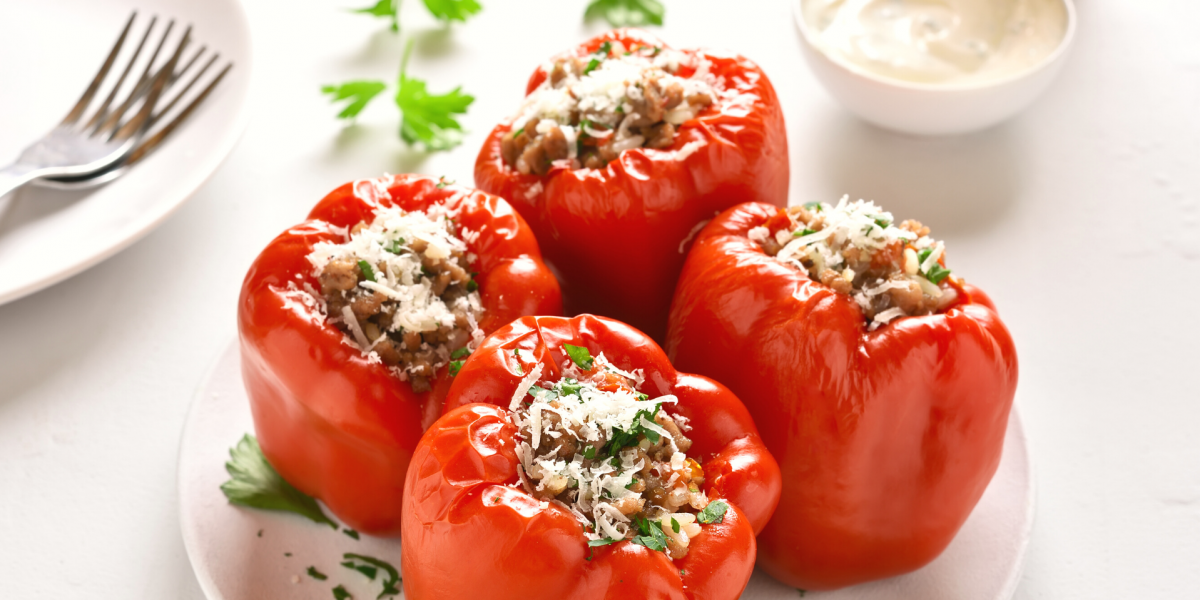 Four red, stuffed bell peppers on a white plate, against a white background.