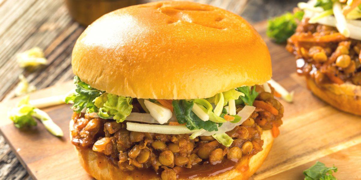 Photo of a lentil sloppy joe sandwich, with lettuce, on a cutting board.