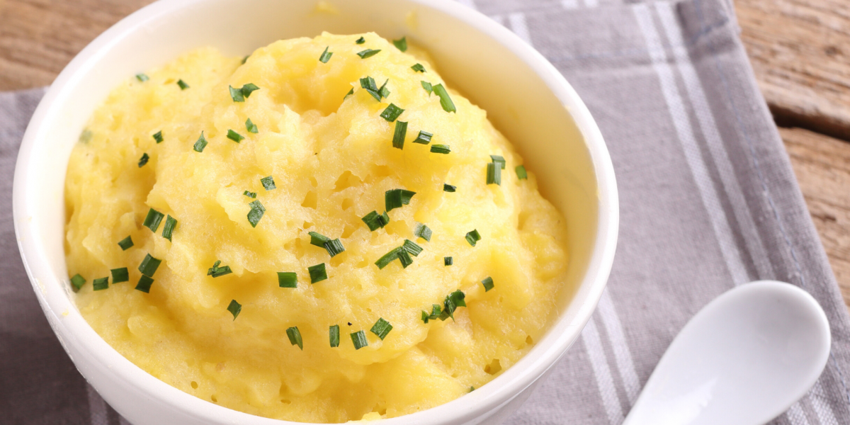 White bowl full of mashed rutabaga, on top of a grey napkin, next to a white spoon.