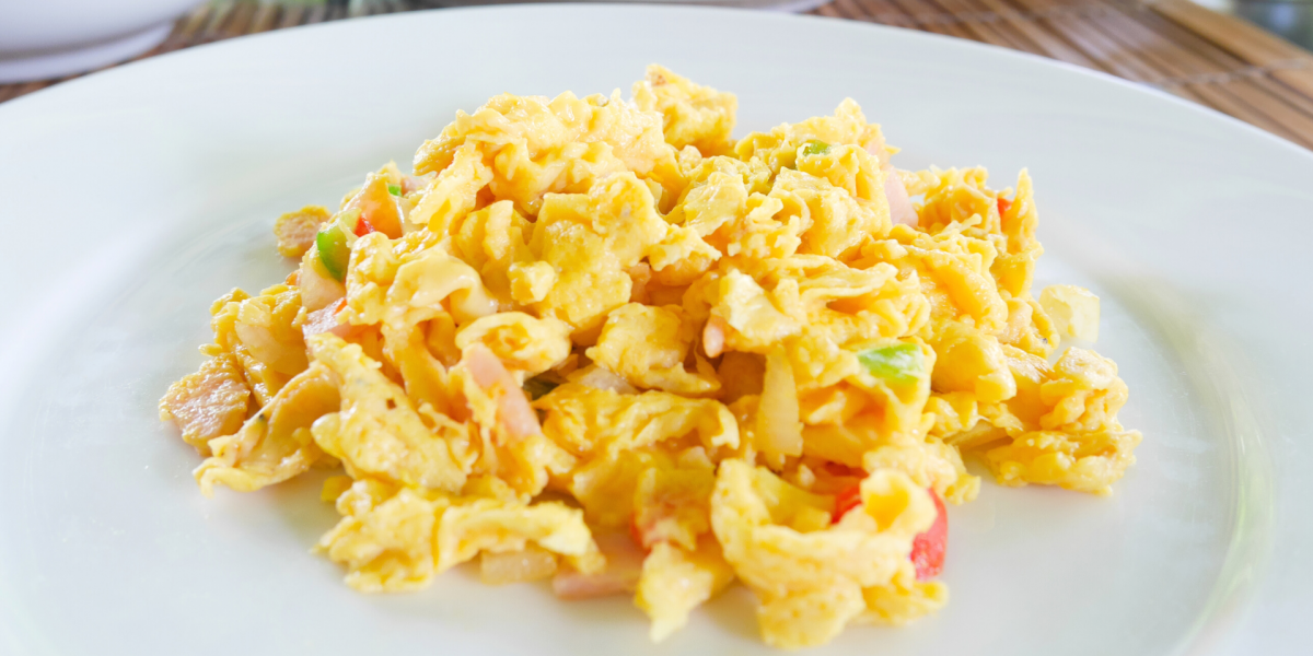 Microwave Breakfast Scramble Recipe Photo. White plate with scrambled eggs on it. Peppers and ham are mixed in with the eggs.