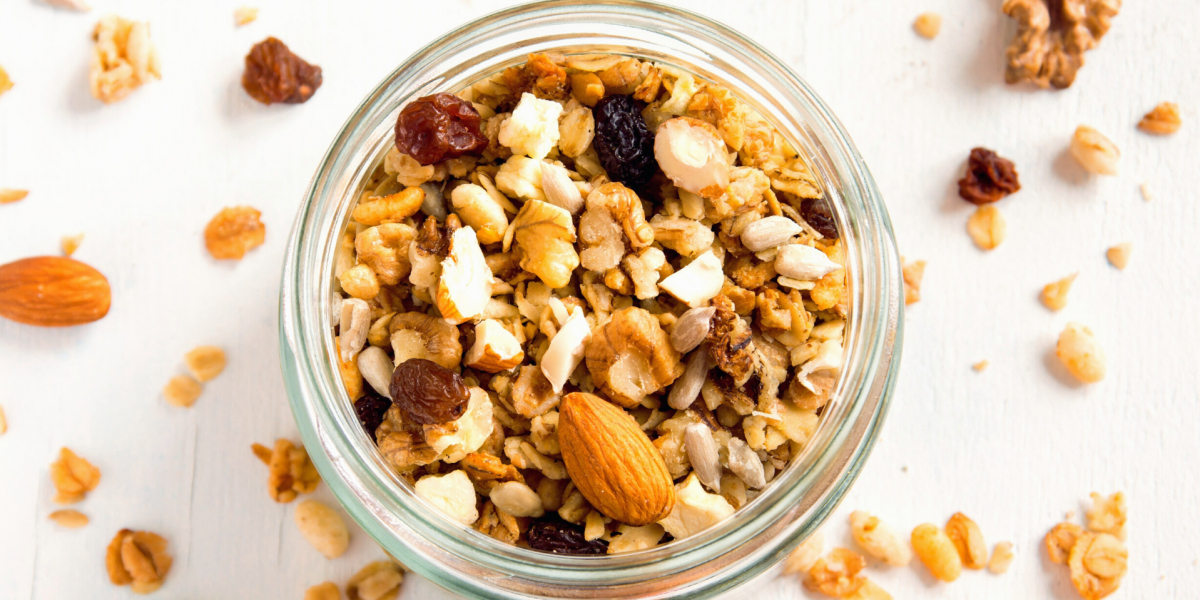 Nutty Granola Recipe Photo. Clear jar full of granola sitting on a white background. Bits of granola are on the table among the jar.