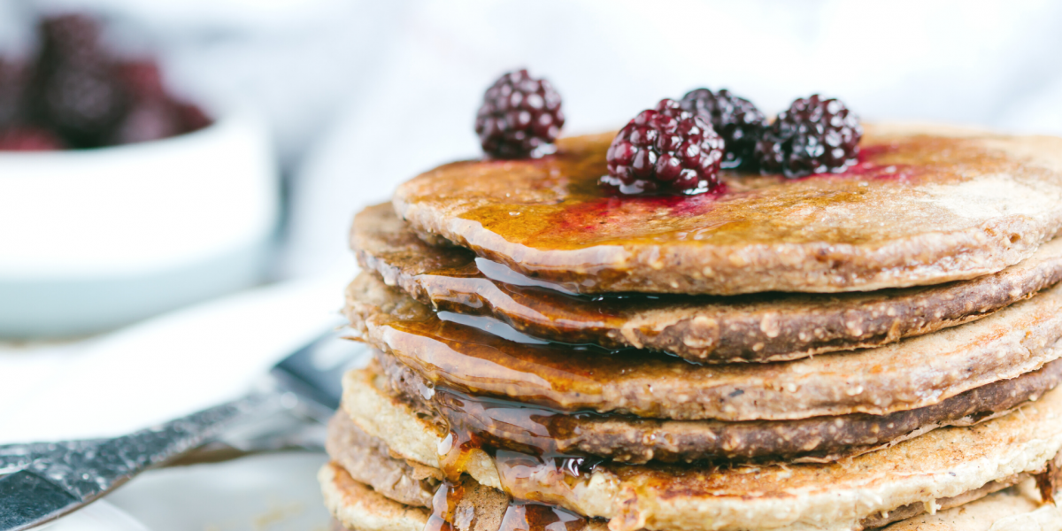 Orange Oatmeal Pancakes Recipe Photo. Stack of pancakes with berries and syrup on top, against a primarily white background.