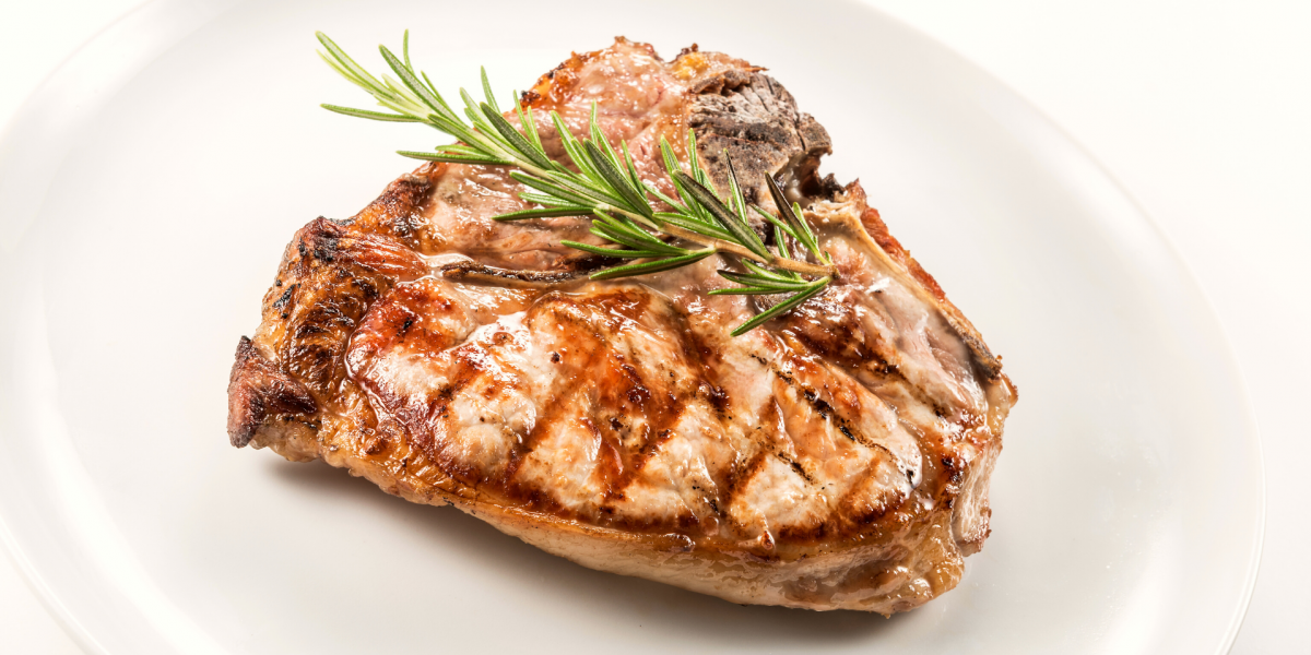 A single pork chop on a white plate, against a white background. Garnished with herbs.
