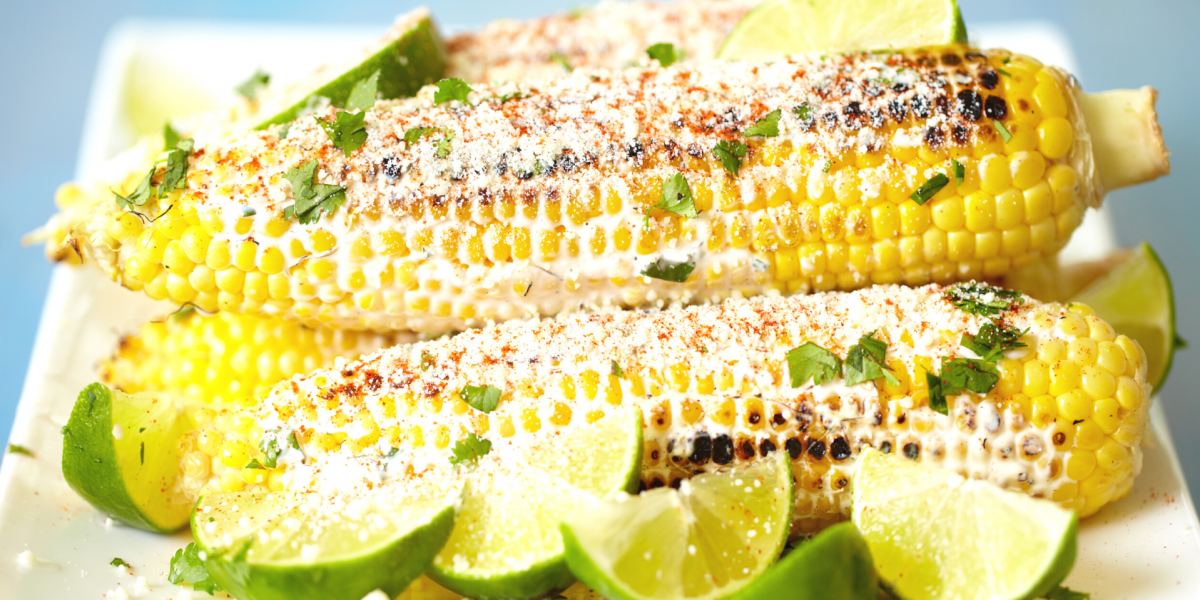 Prepared Corn on the Cob (Elote Preparado) Recipe Photo. Seasoned cooked cobs of corn on a white plate, with a blue background.