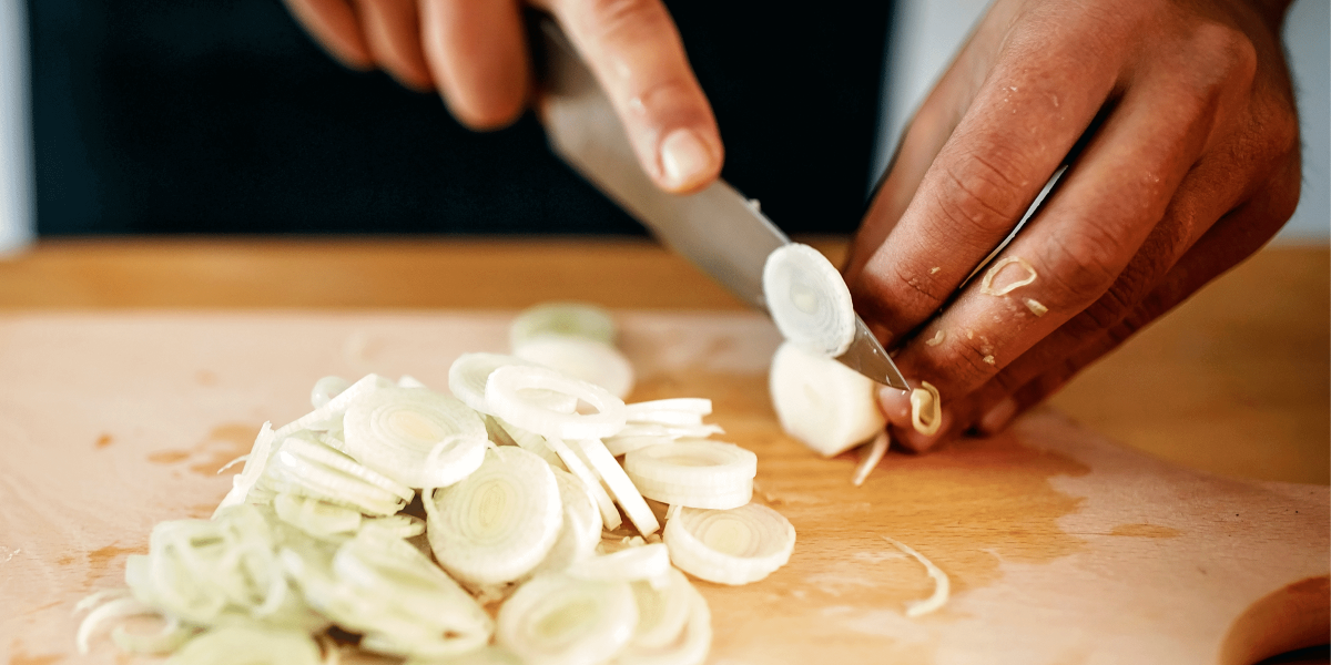 Hands cutting green onion on wooden chopping board