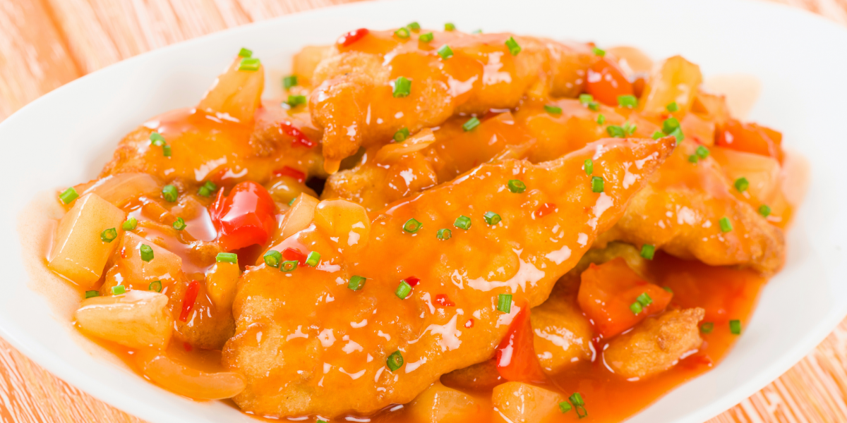 Sheet pan sweet and sour chicken served up in a white dish, against a background of light tan wood.