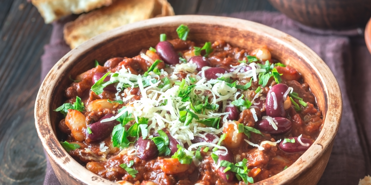 Wooden bowl of turkey and bean chili, topped with herbs and cheese.