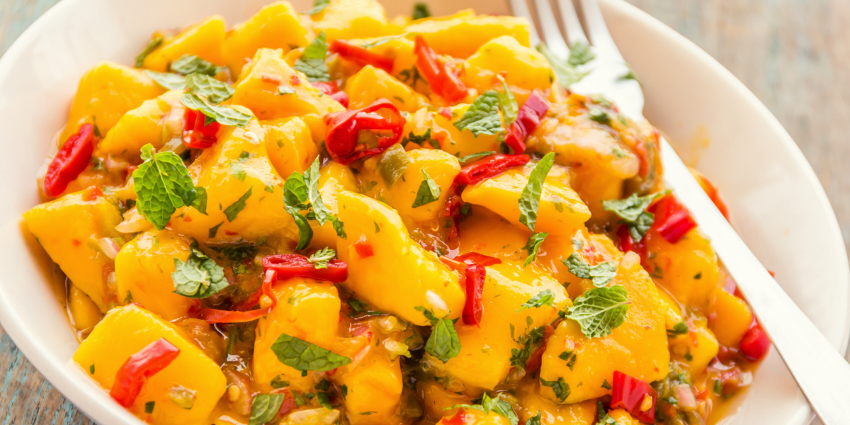 Tropical bean salad, with mango, pepper and tomato. Food is in a white bowl.