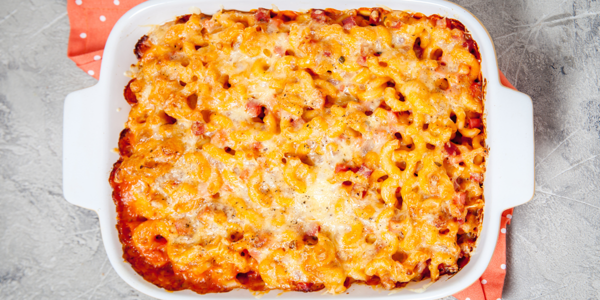 A white ceramic baking pan with freshly baked macaroni and cheese in it, against a grey background.