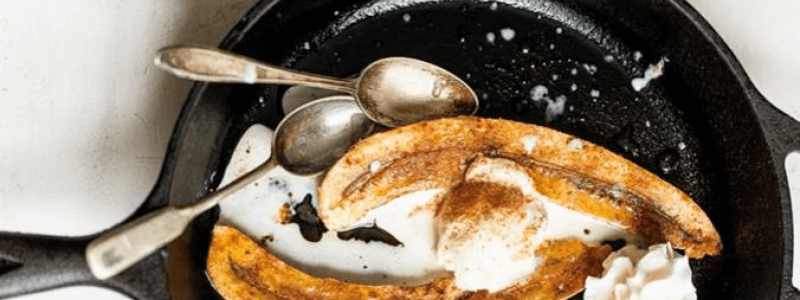 bananas with two vintage spoons in cast iron pan with whipped cream