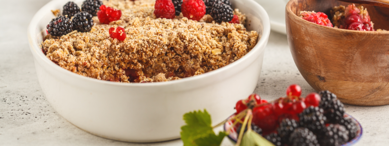 Banana Blueberry Oatmeal Bake Recipe Photo. Oatmeal and berry bake/crumble in white baking dish, against a mostly white background.
