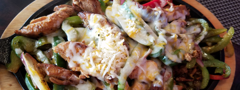 Bell Peppers, Unstuffed Recipe Photo. Meat and bell peppers covered in cheese. Background is black, with a circle of wood around outside of the plate.