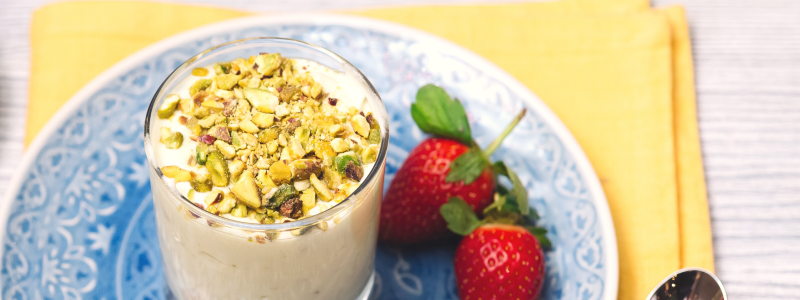 Berries and Pistachio Parfait Recipe Photo. Cup of yogurt is in a blue plate with some berries next to it; under the plate is a yellow napkin. Background is light grey.
