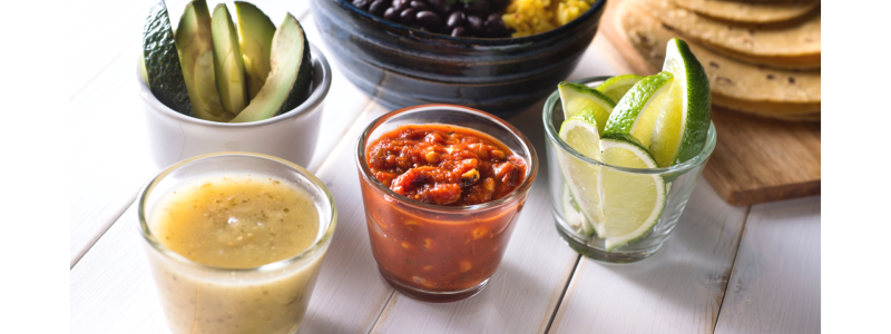 Black Bean Tacos Recipe Photo. Ingredients for making tacos are laid out in bowls, with corn tortillas to the side. Table is white.