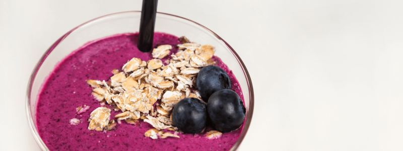 Smoothie with blueberries, oats, milk, hemp seeds, and banana. Against a white background.