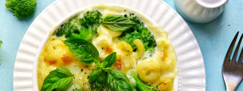 A plate of Baked Broccoli Mac and Cheese, on a white plate, against a blue background.