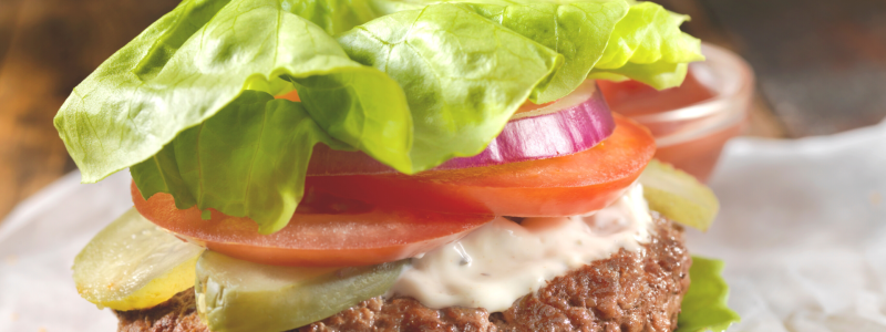 A classic California Style Burger, but wrapped in lettuce instead of a bun. Blurred and mostly white background.