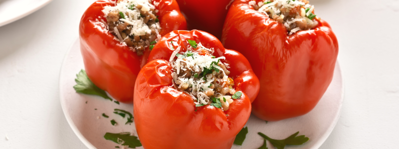 Four red,  stuffed bell peppers on a white plate, against a white background.