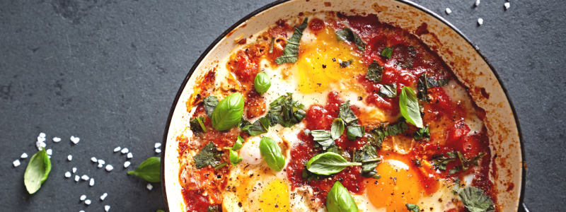 Eggs in Tomato Sauce with Chickpeas and Spinach Recipe Photo. Food is in a white pan against a grey background. Bowl of salt is to the side. 