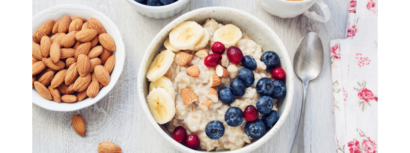 Recipe photo for fruity and creamy no-cook oatmeal. White bowls and light grey background. Almonds and fruit in smaller bowls.