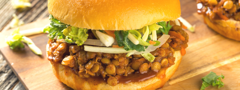 Photo of a lentil sloppy joe sandwich, with lettuce, on a cutting board.