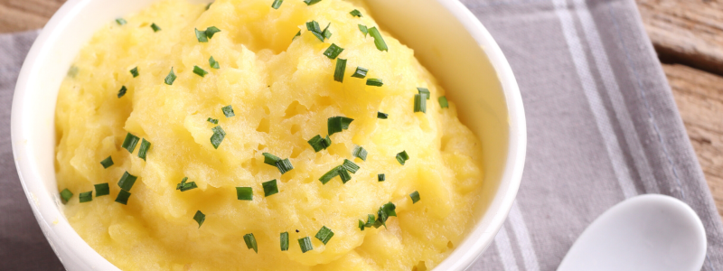 White bowl full of mashed rutabaga, on top of a grey napkin, next to a white spoon.