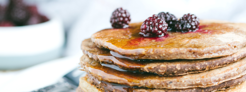 Orange Oatmeal Pancakes Recipe Photo. Stack of pancakes with berries and syrup on top, against a primarily white background.