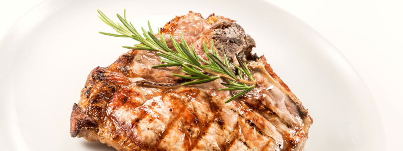 A single pork chop on a white plate, against a white background. Garnished with herbs.