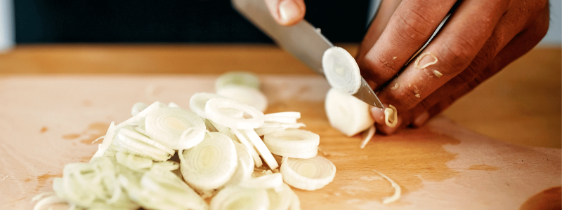 Hands cutting green onion on wooden chopping board