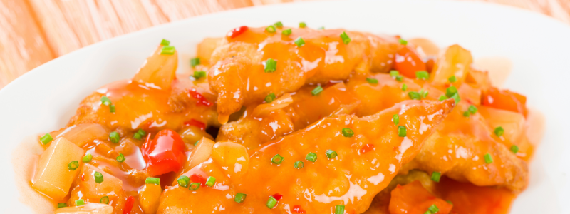 Sheet pan sweet and sour chicken served up in a white dish, against a background of light tan wood.