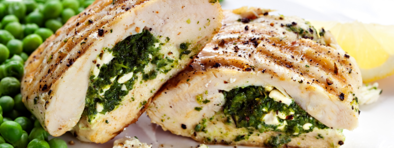 Spinach Stuffed Chicken Breasts with Tomato and Feta Recipe Photo. Grilled, stuffed chicken next to some peas, on a white plate.