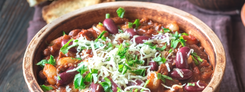 Wooden bowl of turkey and bean chili, topped with herbs and cheese.