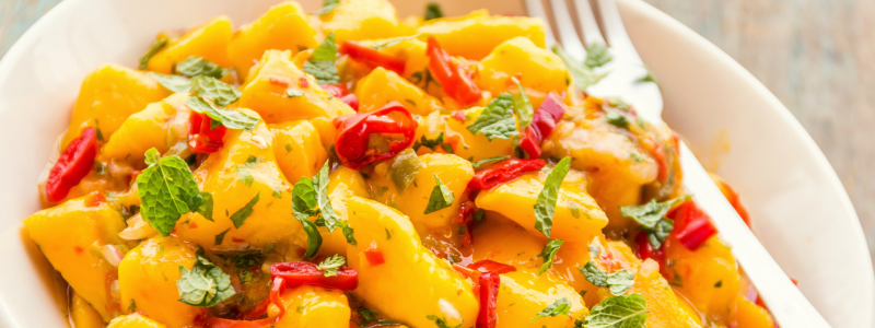 Tropical bean salad, with mango, pepper and tomato. Food is in a white bowl.
