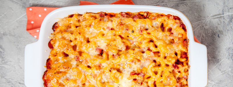 A white ceramic baking pan with freshly baked macaroni and cheese in it, against a grey background.