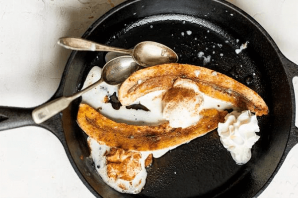 bananas with two vintage spoons in cast iron pan with whipped cream