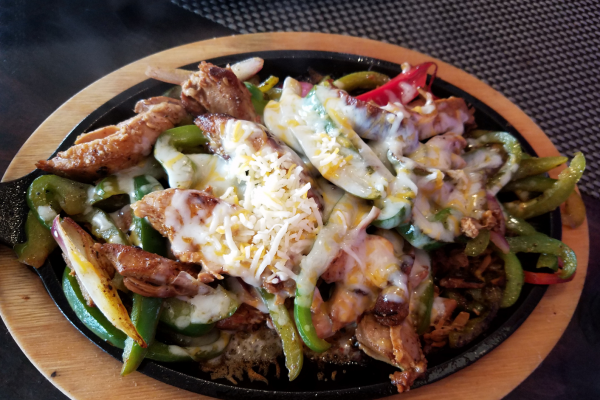 Bell Peppers, Unstuffed Recipe Photo. Meat and bell peppers covered in cheese. Background is black, with a circle of wood around outside of the plate.