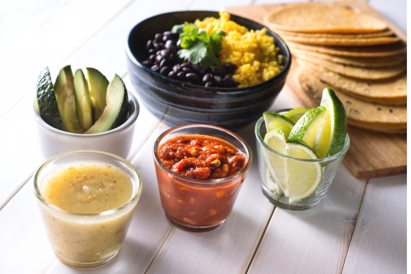 Black Bean Tacos Recipe Photo. Ingredients for making tacos are laid out in bowls, with corn tortillas to the side. Table is white.