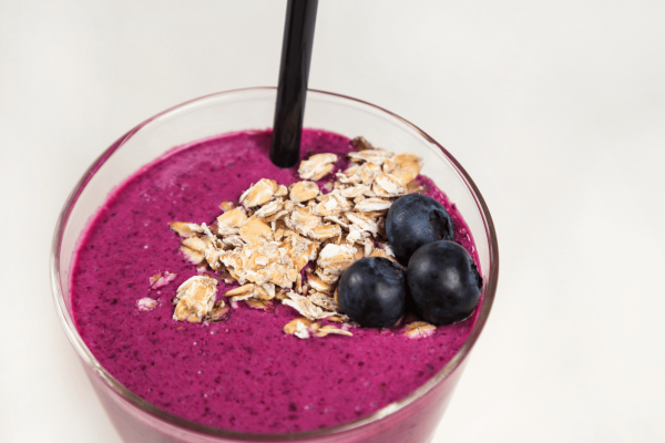 Smoothie with blueberries, oats, milk, hemp seeds, and banana. Against a white background.