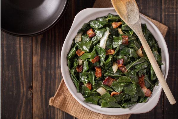 Braised greens in white bowl, with wooden spoon across the top of the dish.