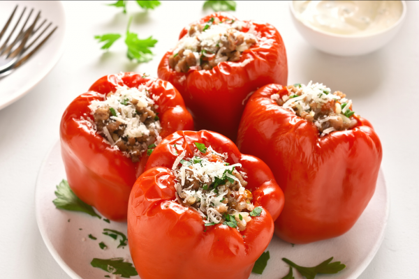 Four red,  stuffed bell peppers on a white plate, against a white background.