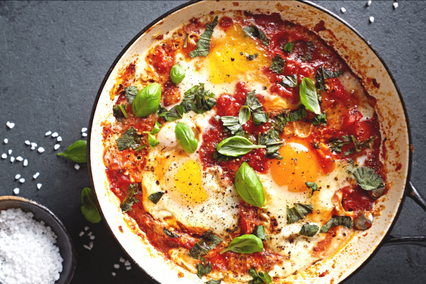 Eggs in Tomato Sauce with Chickpeas and Spinach Recipe Photo. Food is in a white pan against a grey background. Bowl of salt is to the side. 