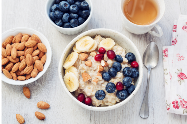 Recipe photo for fruity and creamy no-cook oatmeal. White bowls and light grey background. Almonds and fruit in smaller bowls.