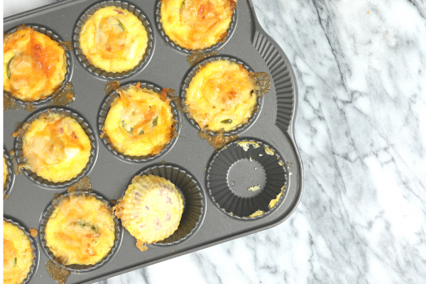 Holiday Brunch Cups in a cupcake-style baking pan. Food is yellow and orange, and background is grey granite.