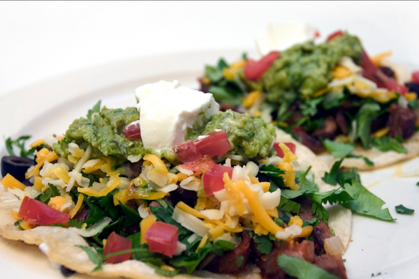 Honduran Enchiladas Recipe Photo. Cheese, greens, tomatoes and beef top two corn tostadas. Plate and background and plate are white.