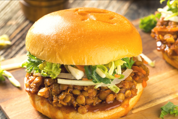 Photo of a lentil sloppy joe sandwich, with lettuce, on a cutting board.