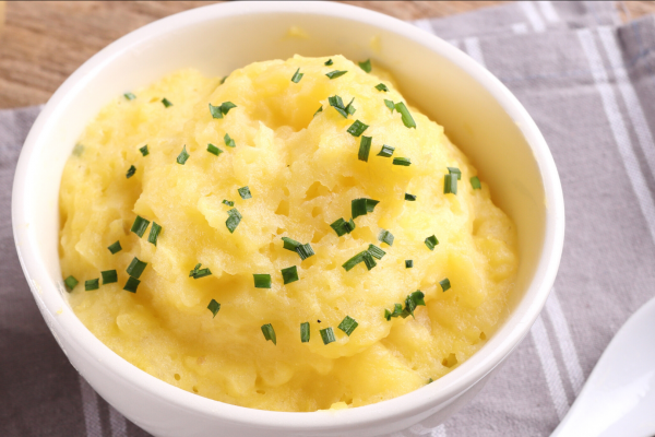 White bowl full of mashed rutabaga, on top of a grey napkin, next to a white spoon.